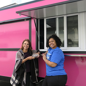 Two women stand outside of a bright pink food truck