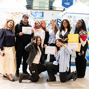 A group of diverse students smiles and poses for a camera