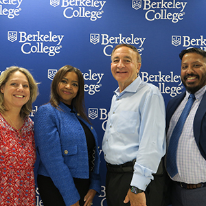 Four diverse people stand in a row and smile in front of a Berkeley College backdrop