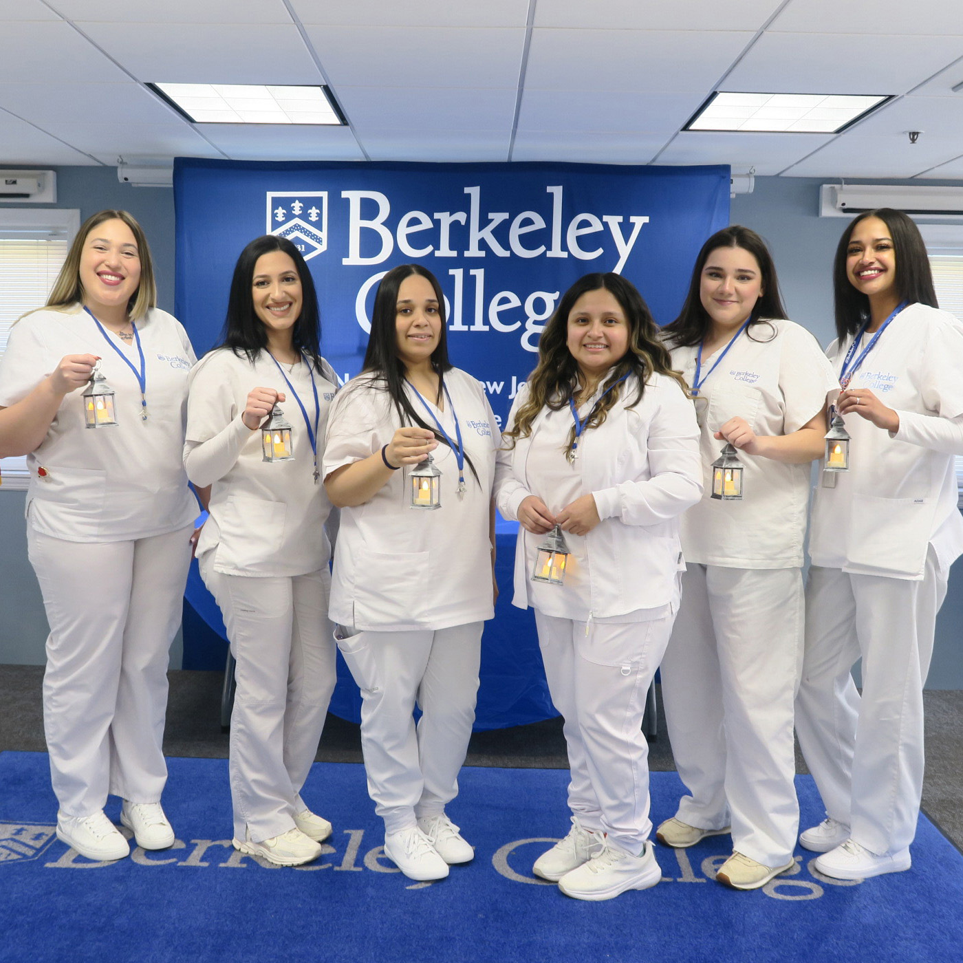 Students in white scrubs pose on a stage.
