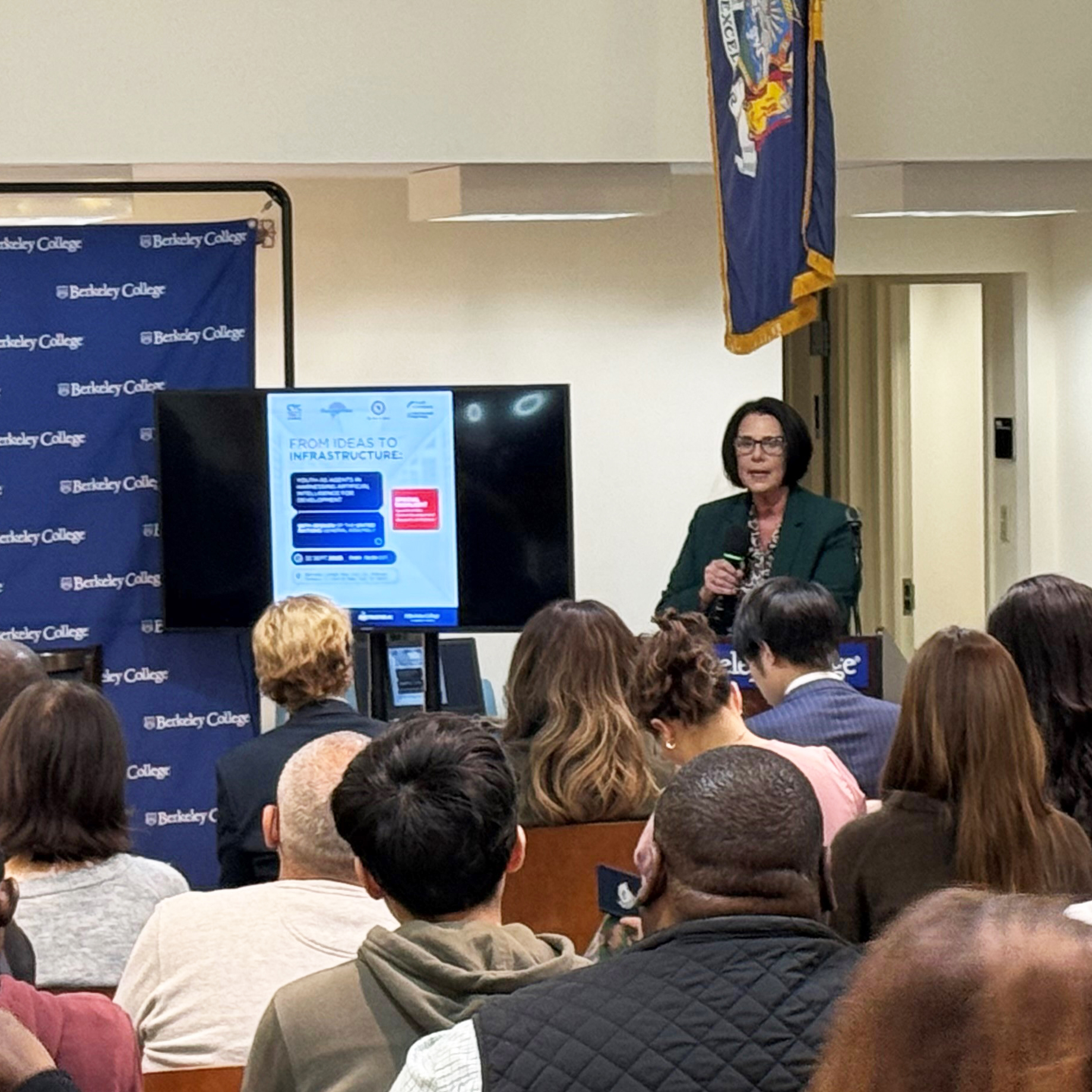 A woman at the podium speaks to a large audience