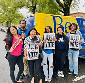 Several people gather in front of a van, each holding signs that express their thoughts and opinions