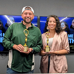 A man and a woman stand next to each other, each holding a golden statue.