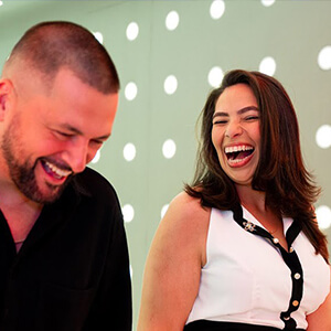 A man and woman are joyfully laughing, standing in a room with glowing polka dot lights on the walls. The mood is light and cheerful.