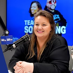 Photo of Carolyn Whitman, A woman in a radio studio smiles while sitting in front of a microphone. Behind her, a screen displays a show's title with two hosts pictured.