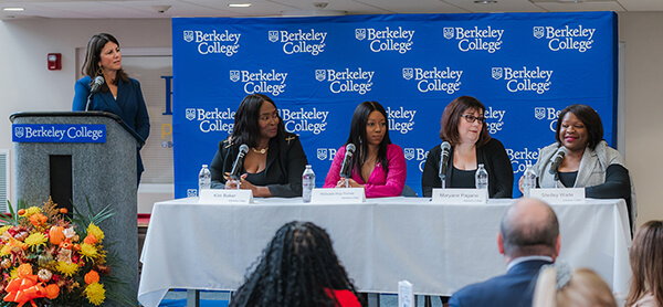 A panel of four women and a women speaker in front of a Berkeley College blue banner