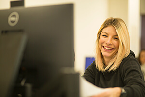 A woman smiling at her desk, focused on her computer screen