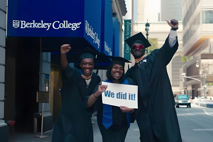 Three graduates in caps and gowns joyfully celebrate holding a We did it! sign outside Berkeley College. They convey happiness and accomplishment.