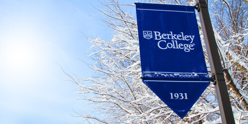 A blue banner displaying Berkeley College and 1931, surrounded by snow-covered trees against a clear sky.