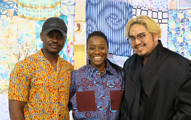 Three designers-in-residence stand and smile in front of a fabric backdrop.