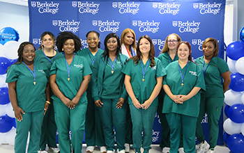 A group of nurses in scrubs stands in front of a backdrop and smiles