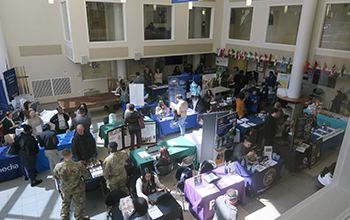 A large auditorium filled with people, tables, and posters.