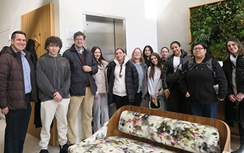 A group of students and staff stands smiling in a white lobby with a couch.