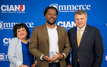 Three people pose in front of a blue backdrop with CIANJ Commerce logos, with the center person holding an award plaque.