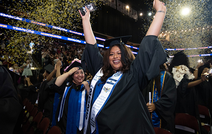 A Berkeley College graduate raises her hands in celebration as confetti falls