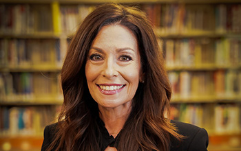 A woman smiles in front of a bookshelf