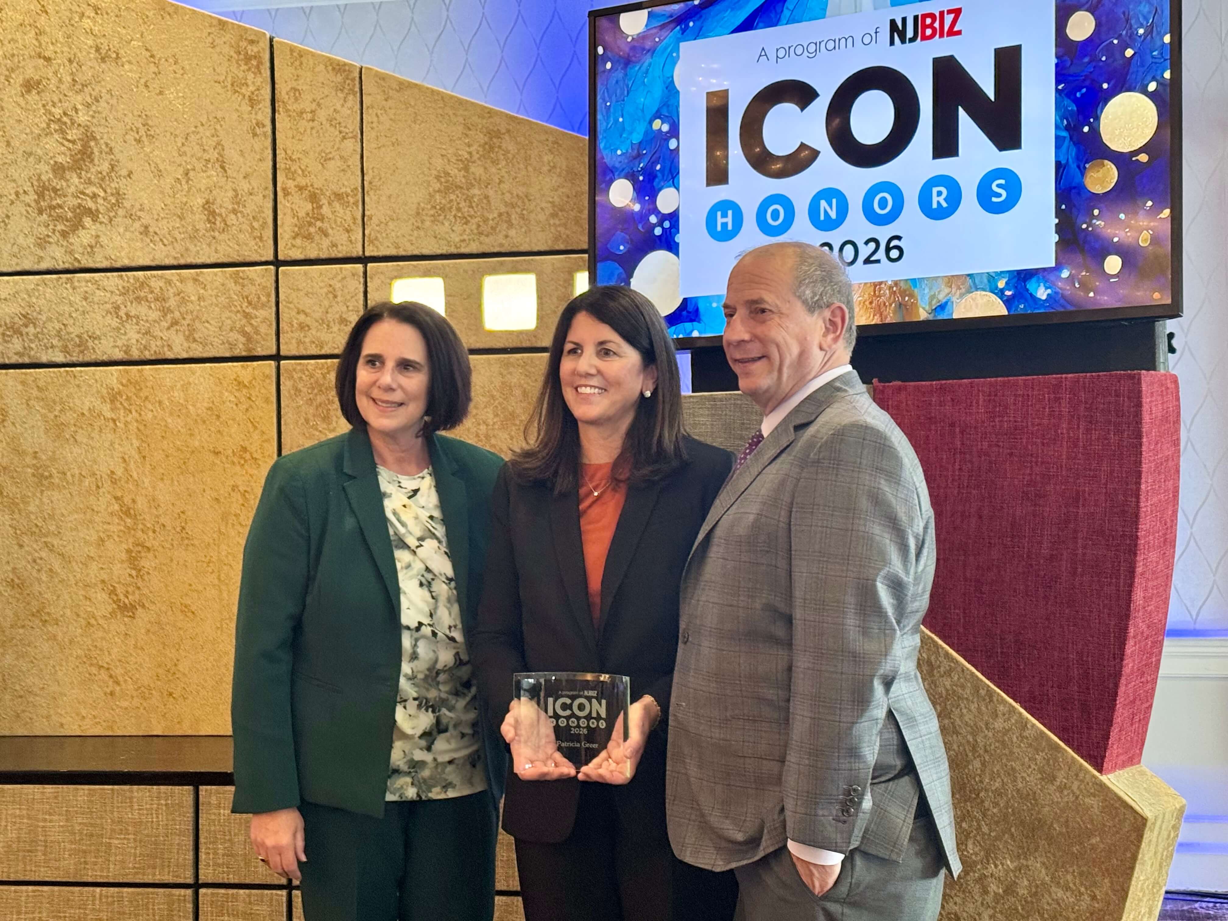 Three people posing with an ICON Honors 2026 award in front of a screen displaying the event's logo at an indoor venue.