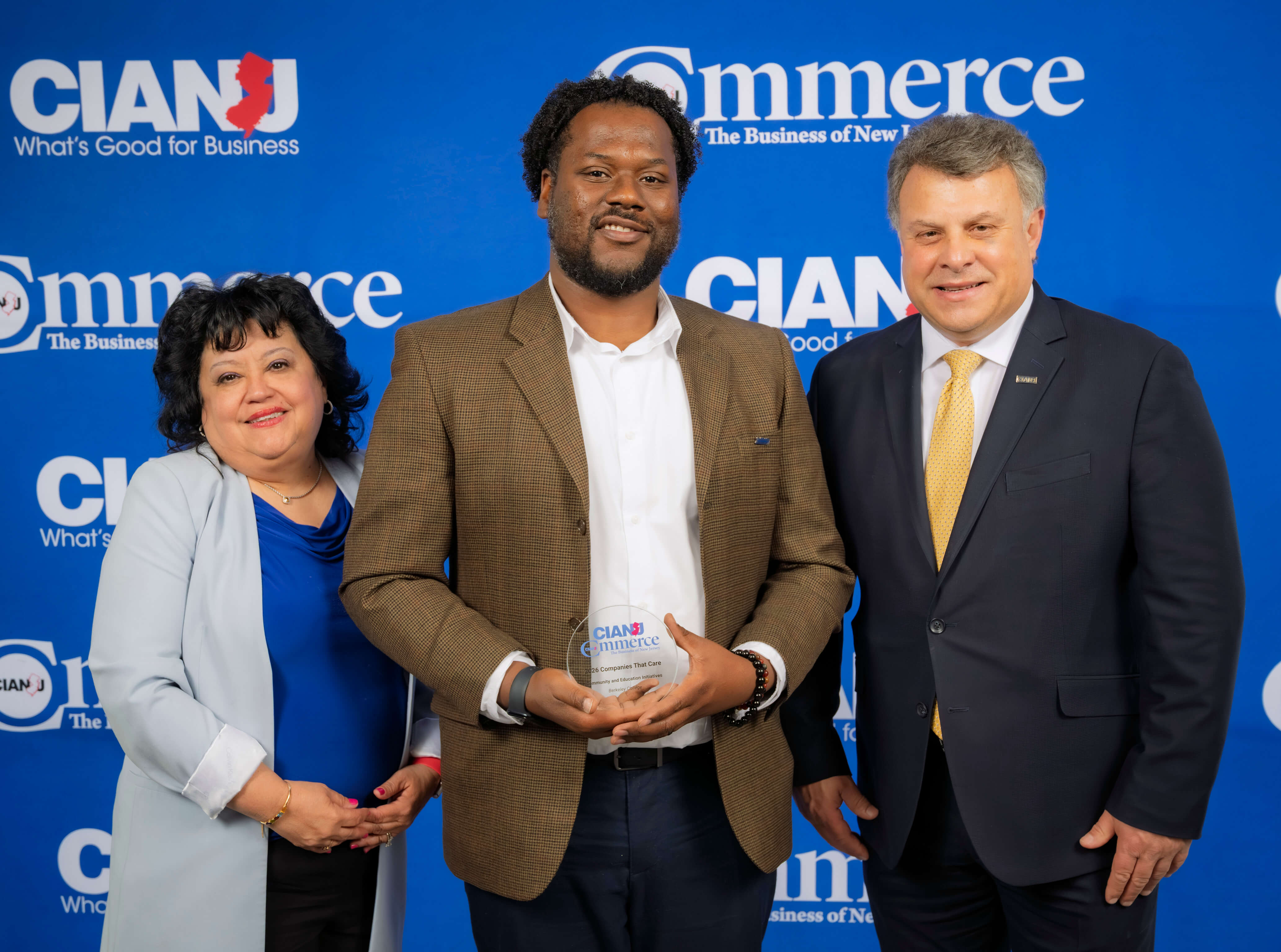 Three people pose in front of a blue backdrop with CIANJ Commerce logos, with the center person holding an award plaque.