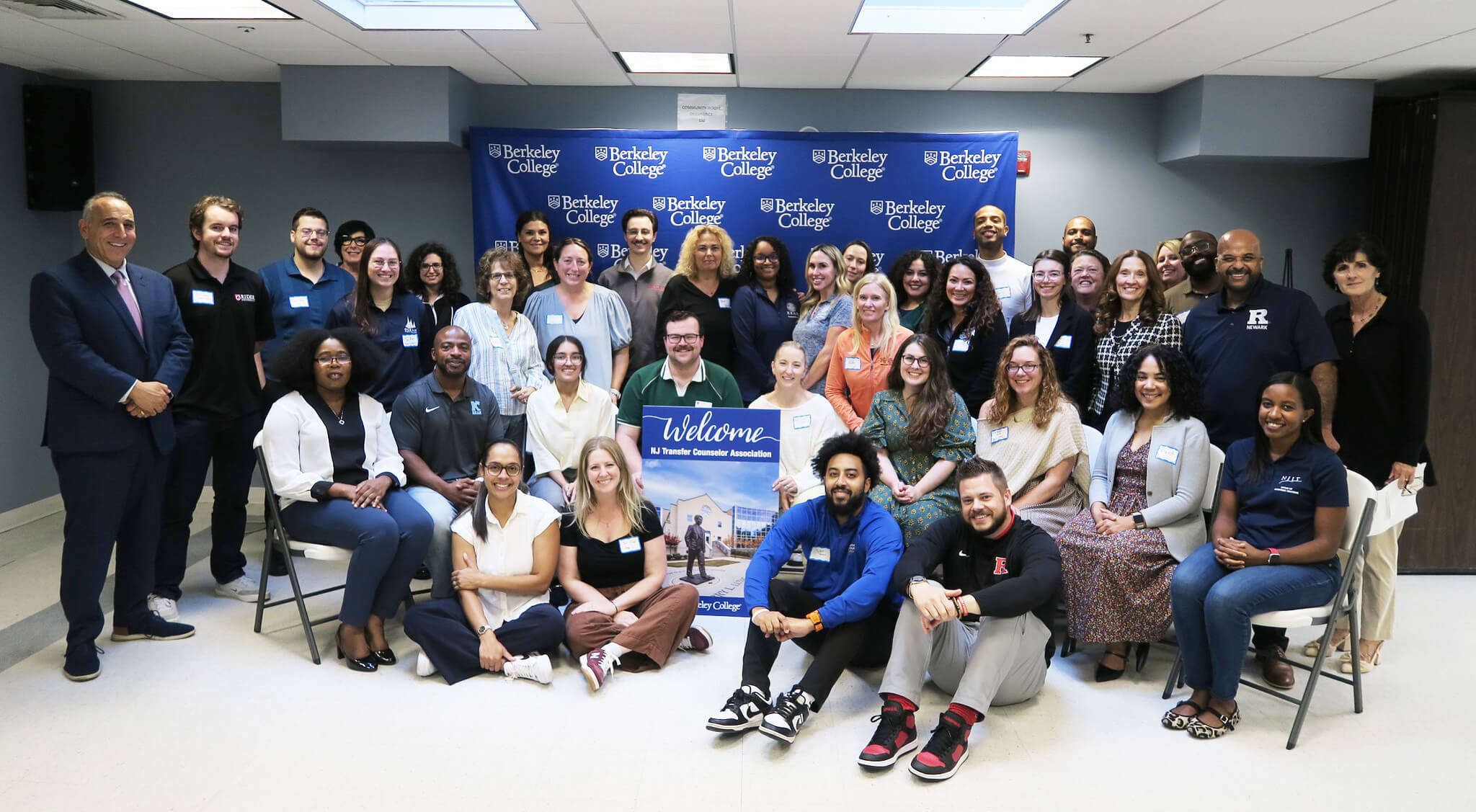 Group photo of college staff and counselors posing beneath a Berkeley College banner with a “Welcome” sign.