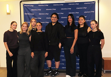 Group of seven young adults standing and posing in front of a Berkeley College backdrop, all dressed in dark casual and semi-formal attire.