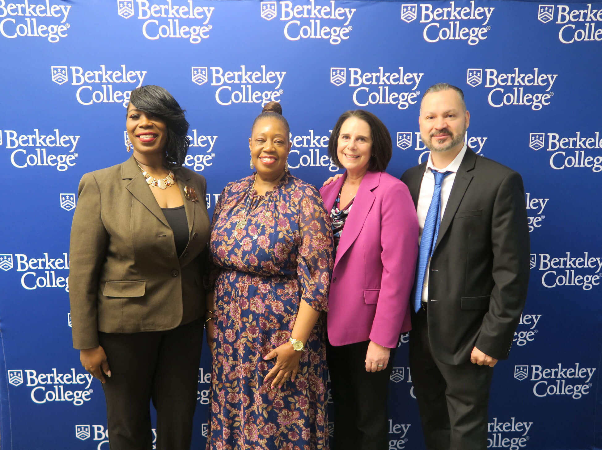 Four people dressed in business attire standing in front of a Berkeley College branded backdrop.