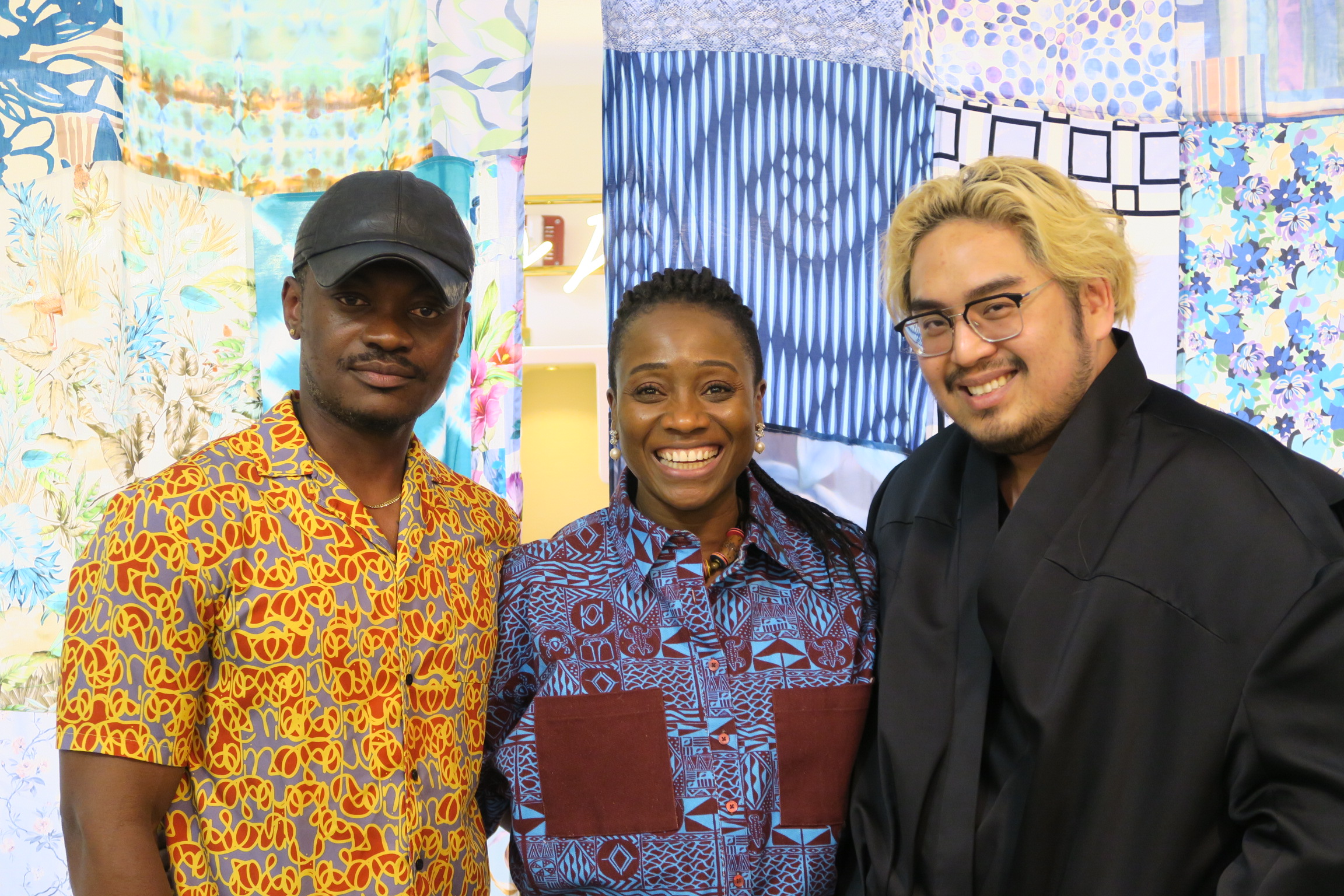 Three designers-in-residence smile and pose for a photo in front of a fabric backdrop