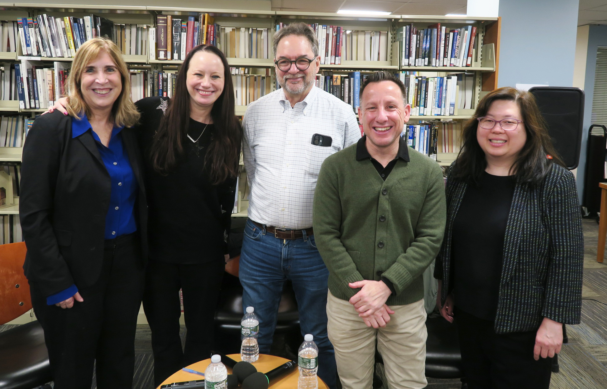 men and women stand and smile in front of a book shelf