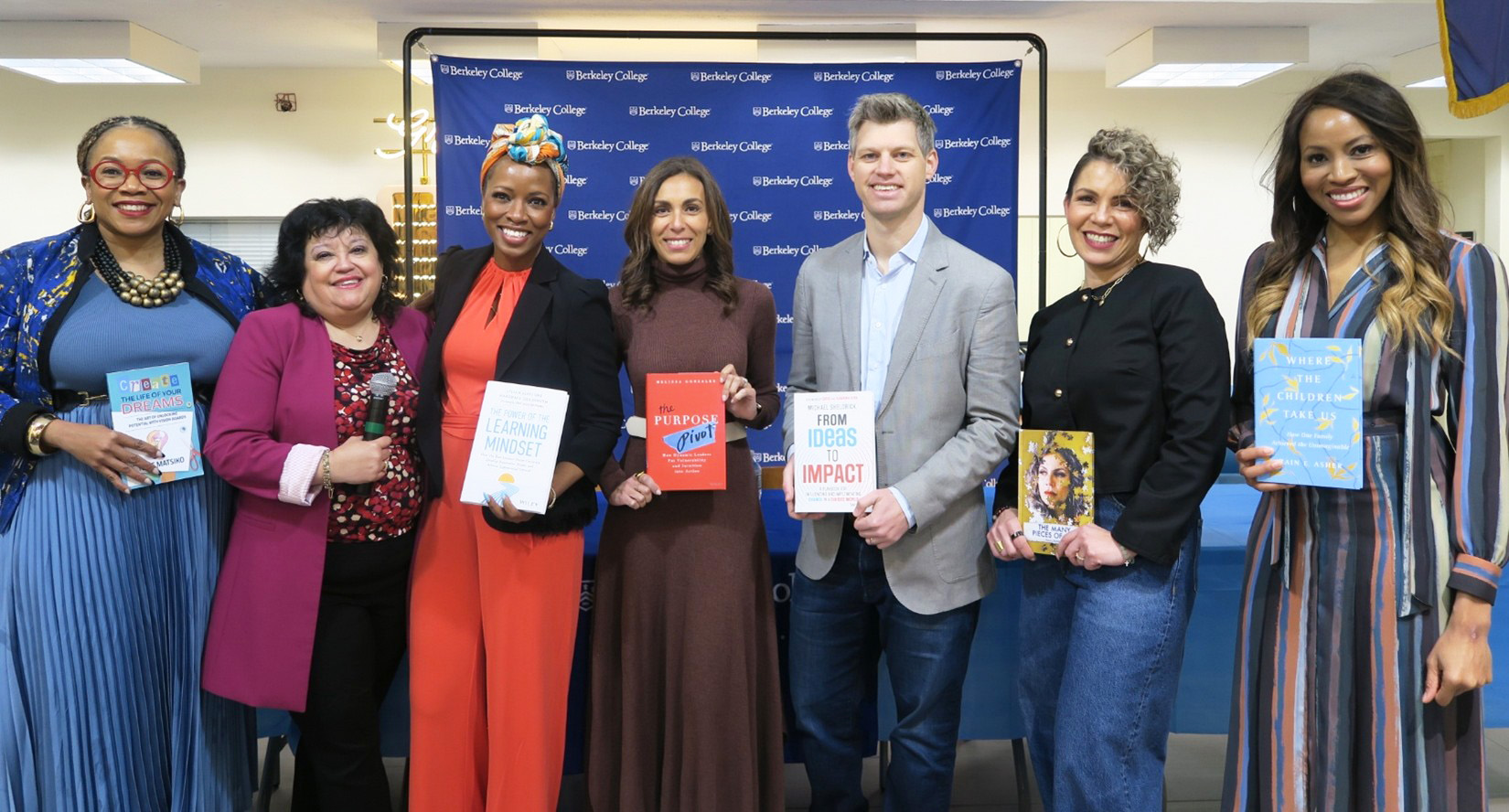 Seven people standing in front of a Berkeley College backdrop, each holding a different book in a group photo.