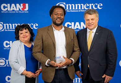 Three people posing at a CIANJ event, with one person holding a CIANJ award, standing against a branded blue backdrop.