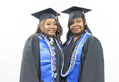 Two graduates wearing black caps, gowns, and blue stoles with "Grad" and "2026" against a white background.