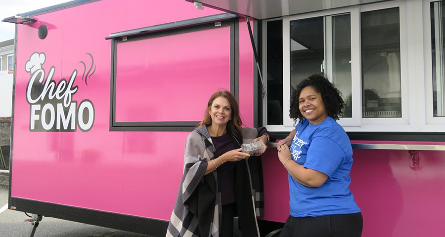 two women stand by a pink food truck