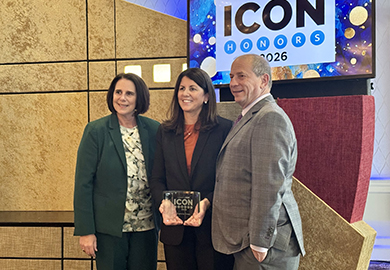 Three people posing indoors with an ICON Honors 2026 award, standing in front of a colorful event sign.