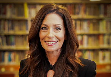 a woman stands in front of a backdrop of books