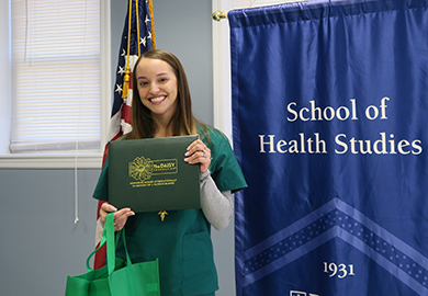 a woman holds a certificate in front of a blue banner