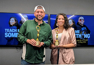 Two people smiling and holding golden awards in front of screens displaying "Teach Me Something" podcast branding.