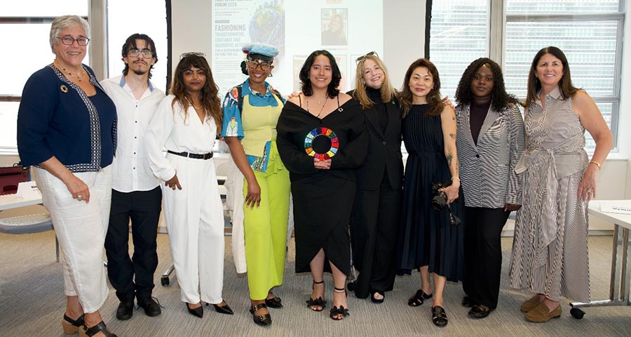 Group of nine individuals standing in a room, smiling and posing for a photo in front of a presentation screen.
