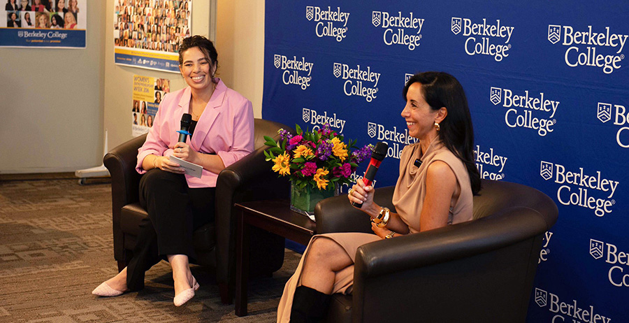 two women sit in front of a blue backdrop with microphones