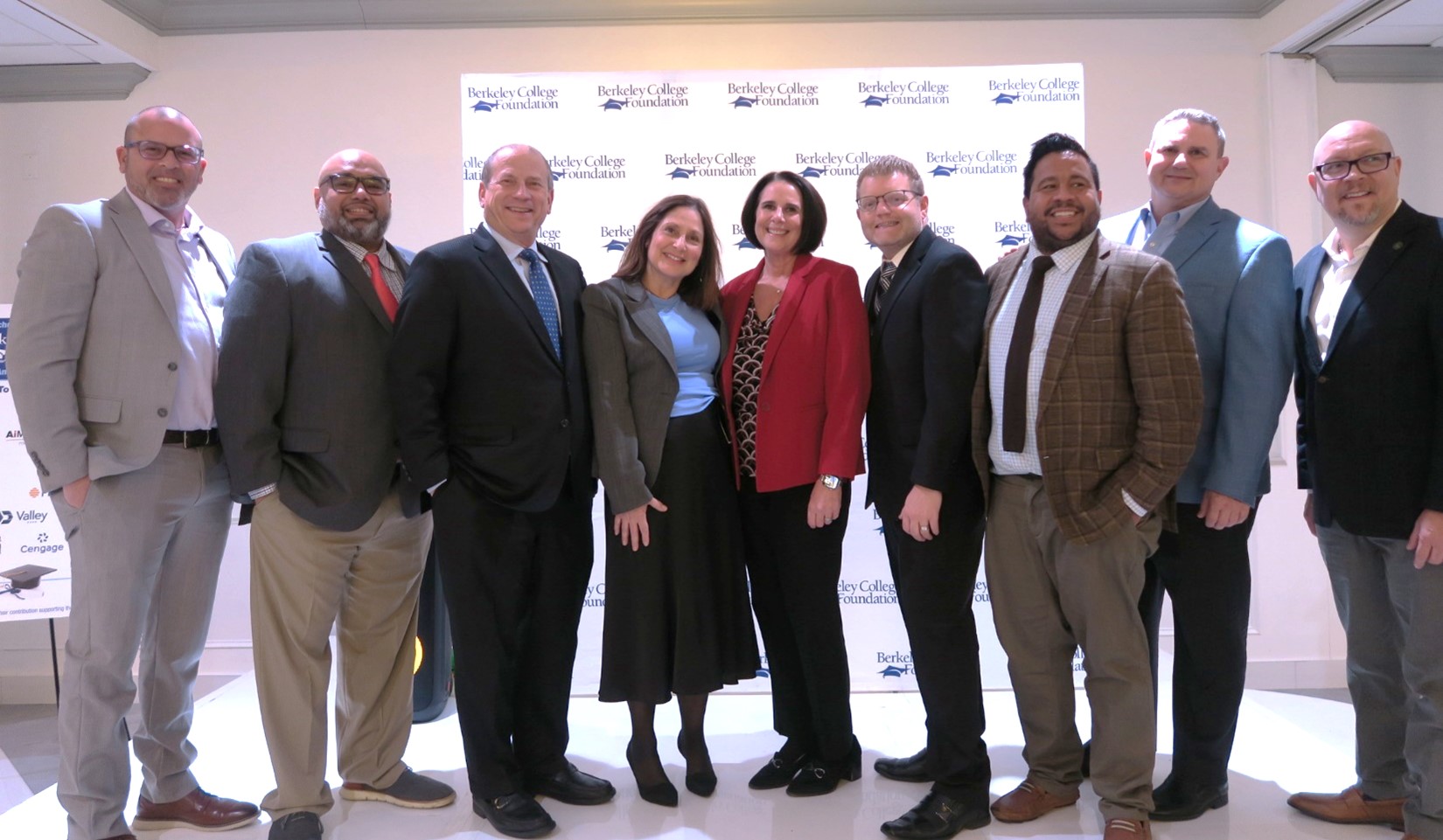 A group of adults stands in a line and smiles for a picture.