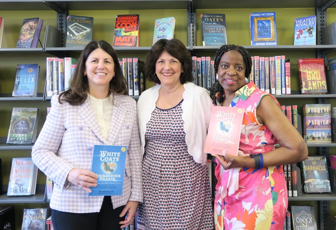 A photo of three diverse women standing in front of a bookshelf.