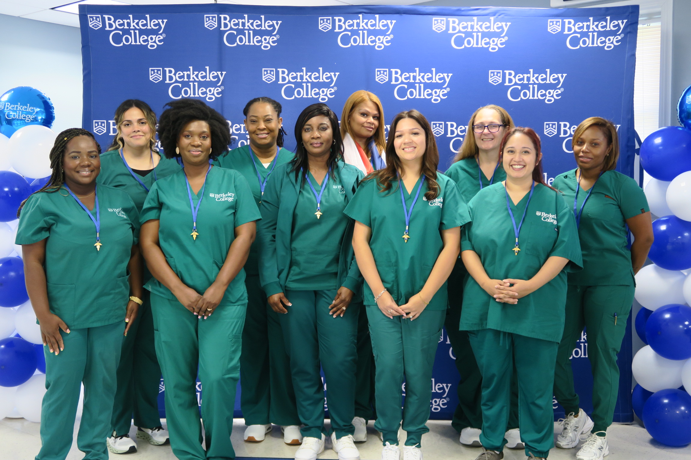 A group of nurses in scrubs standing in front of a backdrop smiling.