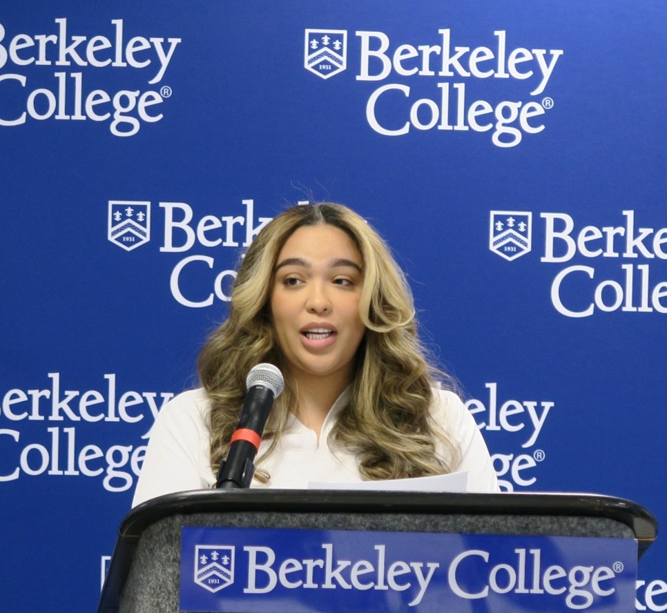 A woman in white scrubs stands at a podium giving a speech