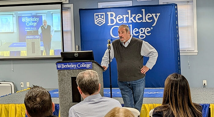 A man stands at a podium, delivering a presentation to an audience at a professional conference