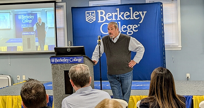 A man stands at a podium, delivering a presentation to an audience at a professional conference